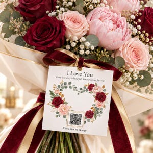 May include: A bouquet of deep red and light pink roses and peonies with baby's breath and eucalyptus. A white square tag tied with a dark red velvet ribbon reads I Love You, Every love story is beautiful, but ours is my favorite, with a QR code.