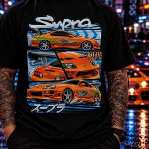 May include: A black short-sleeve t-shirt featuring a graphic print of an orange sports car in three different angles. The design includes the text Supra, Japanese characters, and a blue background element. The car has a rear spoiler and silver wheels.