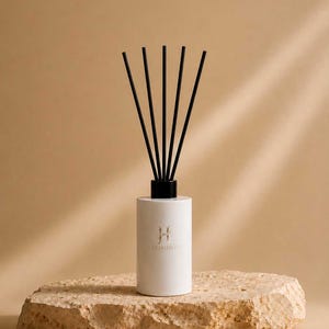 Può includere: Un flacone diffusore a bastoncini cilindrico bianco con un tappo nero e cinque sottili bastoncini neri inseriti. Il flacone presenta un logo dorato con la lettera H e la scritta HARMONICS stampata sul davanti. Il diffusore poggia su una pietra.
