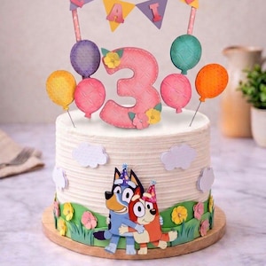 Puede incluir: Un set de decoración para tartas con un número tres grande de color rosa, globos coloridos y una guirnalda con el nombre LAIS. Incluye dos personajes de perros de dibujos animados con gorros de fiesta, recortes de césped y flores pequeñas.