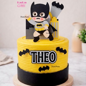 Pode incluir: Um conjunto de topo de bolo amarelo e preto com um personagem de super-herói em desenho animado com máscara e capa pretas, um horizonte urbano amarelo e silhuetas de morcegos pretos. O nome THEO é exibido em letras pretas e brancas.