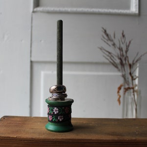May include: A green wooden ring holder with a floral pattern and a silver metal top. The holder is on a wooden surface.