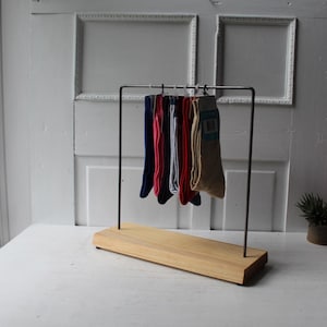 May include: A wooden and metal sock display stand holding several pairs of socks in various colors. The socks are navy blue, pink, red, gray, and beige. The stand has a rectangular wooden base and a metal frame.