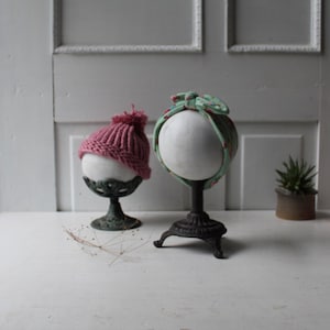 May include: Two fabric headbands displayed on black metal stands. One headband is pink and the other is green with a floral pattern.
