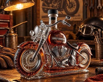 Puede incluir: Un decantador de vidrio transparente con forma de motocicleta que contiene un líquido de color ámbar. El tanque de combustible presenta el texto MOTOR HARLEY-DAVIDSON COMPANY y la base está grabada con HARLEY-DAVIDSON. Tiene manubrios y ruedas cromados.
