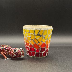 May include: A mosaic glass votive candle holder with a gradient of yellow, orange, and red hues. A beaded lizard figurine with red, purple, and green beads is next to the candle holder. The candle holder is approximately 3 inches tall.