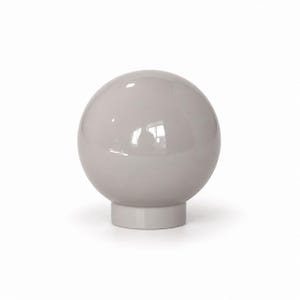 May include: A smooth, glossy, light taupe spherical object resting on a cylindrical base. The surface of the sphere is reflective, showing a subtle highlight from a light source. The entire piece is a uniform, solid, neutral color throughout.