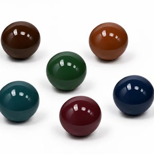 May include: A collection of six smooth, spherical objects with a high-gloss finish. The spheres are colored in dark brown, light brown, forest green, teal, deep burgundy, and navy blue, each reflecting light on their polished, rounded surfaces.