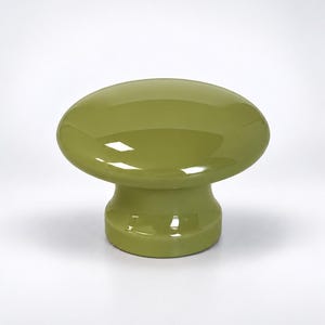 May include: A solid olive green cabinet knob with a smooth, glossy finish. The knob features a wide, rounded top surface that tapers down into a cylindrical base, creating a mushroom-like shape with reflective highlights on the surface.