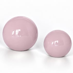 May include: Two smooth, spherical objects with a glossy, light pink finish. The spheres are of different sizes, with one noticeably larger than the other. Both items feature a reflective surface that catches light, creating bright white highlights.