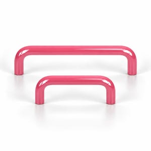 May include: Two U-shaped cabinet pulls in a vibrant, glossy pink finish. The handles feature a smooth, rounded design with a tubular construction. One pull is significantly longer than the other, both displaying a consistent bright pink color.
