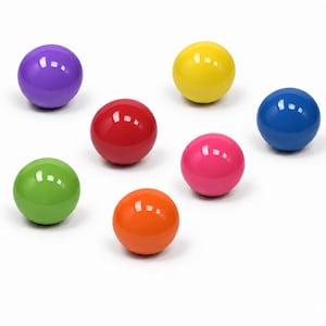 Può includere: Una collezione di sette sfere lisce in una varietà di colori solidi e lucidi, tra cui viola, giallo, blu, rosso, rosa, verde e arancione. Ogni sfera presenta una superficie riflettente che cattura la luce creando un punto luminoso.