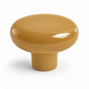 May include: A smooth, mustard yellow cabinet knob with a rounded, mushroom-shaped top and a cylindrical base. The surface has a glossy, reflective finish that catches the light, creating a clean and simple silhouette for furniture hardware.