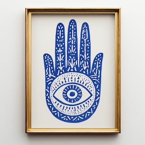 May include: A framed wall art print featuring a bold blue Hamsa hand illustration on a white background. The hand design includes intricate white patterns and a central eye motif, all enclosed within a simple, thin gold-colored frame.