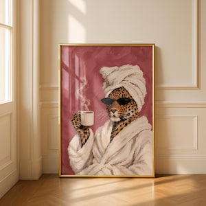 May include: A framed wall art print featuring a leopard wearing a white towel wrapped around its head and a white bathrobe. The leopard wears black sunglasses and holds a white mug with rising steam against a textured dark red background.