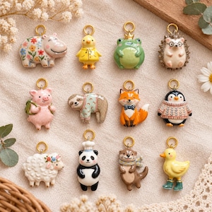May include: A collection of twelve ceramic animal charms with gold-tone metal loops. The figures include a floral hippo, yellow chick, green frog, hedgehog, pig, sloth, fox, penguin, sheep, panda chef, otter, and a duck in green boots.