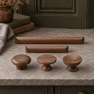 May include: A collection of five dark brown wooden cabinet hardware pieces, including two rectangular bar pulls with beveled edges and three distinct circular knobs with varying profiles, all featuring a smooth, natural wood grain finish.
