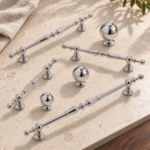 May include: A collection of polished chrome cabinet hardware including three elongated bar pulls with decorative spindle detailing and three spherical knobs. Each piece features a reflective metallic finish and a sturdy mounting base.