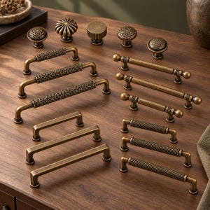 May include: A collection of antique brass cabinet hardware including five round knobs with various textures and ten drawer pulls in different lengths featuring hammered, knurled, and smooth finishes with rounded ends.