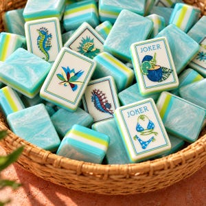 May include: A collection of rectangular mahjong tiles with a marbled light blue and white finish, featuring green and white striped sides. The tiles display various illustrations including a seahorse, a lotus flower, and two tiles labeled JOKER.