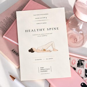 Peut inclure: Un livret d'instructions couleur crème intitulé The Practice Papers Paper No. 003 Mobility Series Healthy Spine. La couverture présente un graphique d'une personne en position de pont avec un bloc sous le dos, et le texte 15 minutes et all levels.