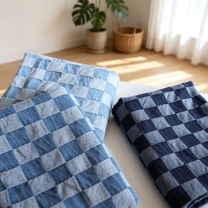 May include: Two folded textile pieces featuring a checkered pattern. One piece displays a light blue and medium blue square grid, while the other piece features a darker navy blue and medium blue square grid, both with a visible woven texture.