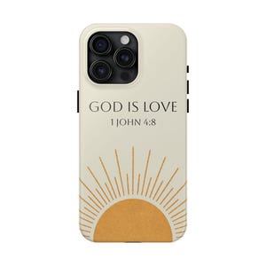 May include: A cream-colored smartphone case featuring a black text graphic that reads GOD IS LOVE 1 JOHN 4:8. Below the text is a stylized mustard yellow semi-circle sun graphic with thin, radiating lines extending upward across the lower portion.