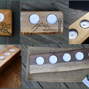 May include: Five wooden candle holders with various engravings. The holders are made of natural wood with a light brown color. The engravings include names, dates, and designs like mountains and ski poles.