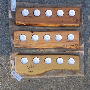 May include: Three wooden candle holders with engraved messages. The top holder says "T&P", the middle holder says "I love you more", and the bottom holder says "J+G 2.19.12".