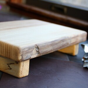 May include: A wooden cutting board with a natural finish and a raised edge. The board has two small legs on the bottom.