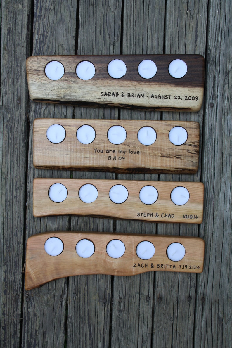 May include: Four wooden candle holders with various dates and names engraved on them. The holders are made of natural wood with a rustic finish. Each holder has four candle slots and is designed to hold tea lights.