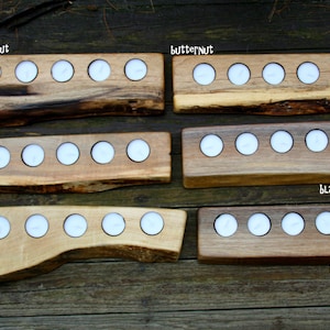May include: Five wooden candle holders with different wood types and finishes. The holders are labeled "Butternut", "Maple", "Black Walnut". Each holder has five or six candle slots.
