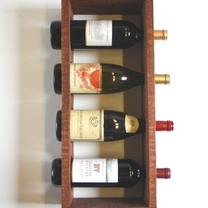 May include: A wooden wine rack holds four bottles of wine. The rack is made of dark brown wood and has four compartments. Each compartment holds a bottle horizontally. The bottles have various label designs and colors.