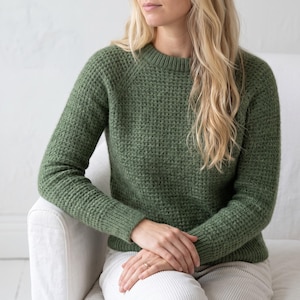 Peut inclure: Un pull vert olive à manches longues avec un motif en maille gaufrée texturée, un col rond et des poignets côtelés. Le vêtement est conçu avec des manches raglan et une coupe ajustée, offrant une texture de maille uniforme sur l'ensemble.