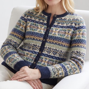 Op de afbeelding: Een gebreid vest met lange mouwen en een veelkleurig Fair Isle-patroon in marineblauw, saliegroen, mosterdgeel en crème. Het kledingstuk heeft een ronde halslijn, een knoopsluiting aan de voorzijde met donkere knopen en geribbelde boorden.