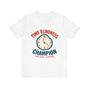 Op de afbeelding: Een wit t-shirt met korte mouwen en een afbeelding van een vervormde klok, met de tekst TIME BLINDNESS CHAMPION in rood en blauw, en de kleinere tekst I'll be there... eventually. in het rood onder de klok.