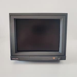 May include: A gray Philips cathode ray tube monitor with a dark screen. The front panel features the Philips logo on the left, a central rectangular panel, and a power button with an indicator light on the right side of the plastic casing.