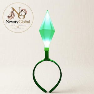 May include: A green plastic headband featuring a tall, diamond-shaped topper that glows with a bright light. The topper is translucent green and tapers to a point at the top, while the headband itself is a solid, dark green colour with teeth.
