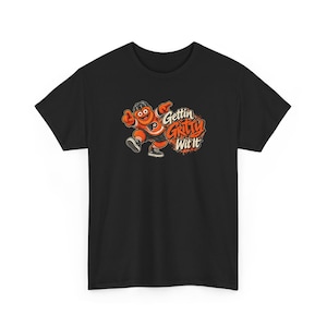 Könnte beinhalten: Ein schwarzes Kurzarm-T-Shirt mit einer Grafik eines orangefarbenen, pelzigen Maskottchens in einem Eishockeytrikot und schwarzen Turnschuhen. Das Maskottchen zeigt mit beiden Händen auf den orange-weißen Schriftzug Gettin Gritty Wit It.