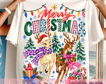 May include: A white t-shirt featuring a colorful graphic with the text Merry Christmas in red and multi-colored letters. The design includes two reindeer, one wearing a plaid scarf and Santa hat, the other with a wreath, plus pine trees and gifts.