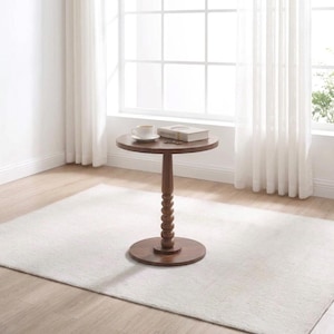 May include: A round brown wooden side table with a single pedestal base featuring a stacked ball design. A white ceramic coffee cup and a closed rectangular book are placed on the flat circular tabletop surface.