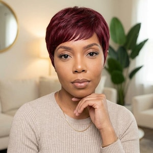 May include: A short, layered pixie cut wig in a deep burgundy red color. The hair is styled with soft, textured layers and short bangs that frame the forehead. The wig features a natural-looking hairline and a smooth, consistent dark red tone.
