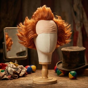Peut inclure: Une perruque orange vif avec une coiffure haute et texturée et une pièce frontale imitant un crâne chauve, présentée sur un support de tête de mannequin de couleur neutre. La perruque présente des sections de cheveux volumineuses et hérissées.