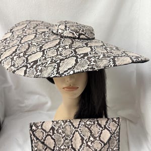 May include: A wide-brimmed hat and a matching rectangular envelope clutch, both featuring a beige and black snakeskin print pattern. The hat has a flat crown and a broad, circular brim, while the clutch has a pointed flap closure.
