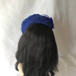 May include: A blue mesh hat with a feather accent. The hat is decorated with small sequins.