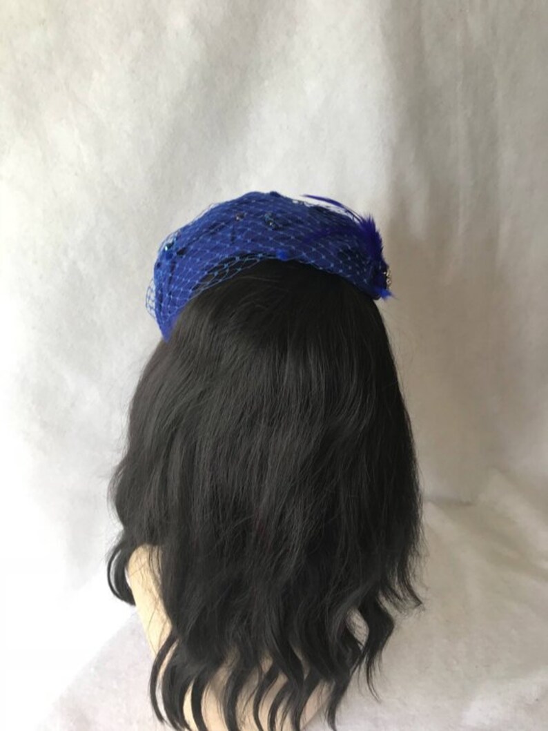 May include: A blue mesh hat with a feather accent. The hat is decorated with small sequins.