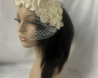May include: A white flower hat with a veil. The hat is made of fabric flowers and has a pearl embellishment.