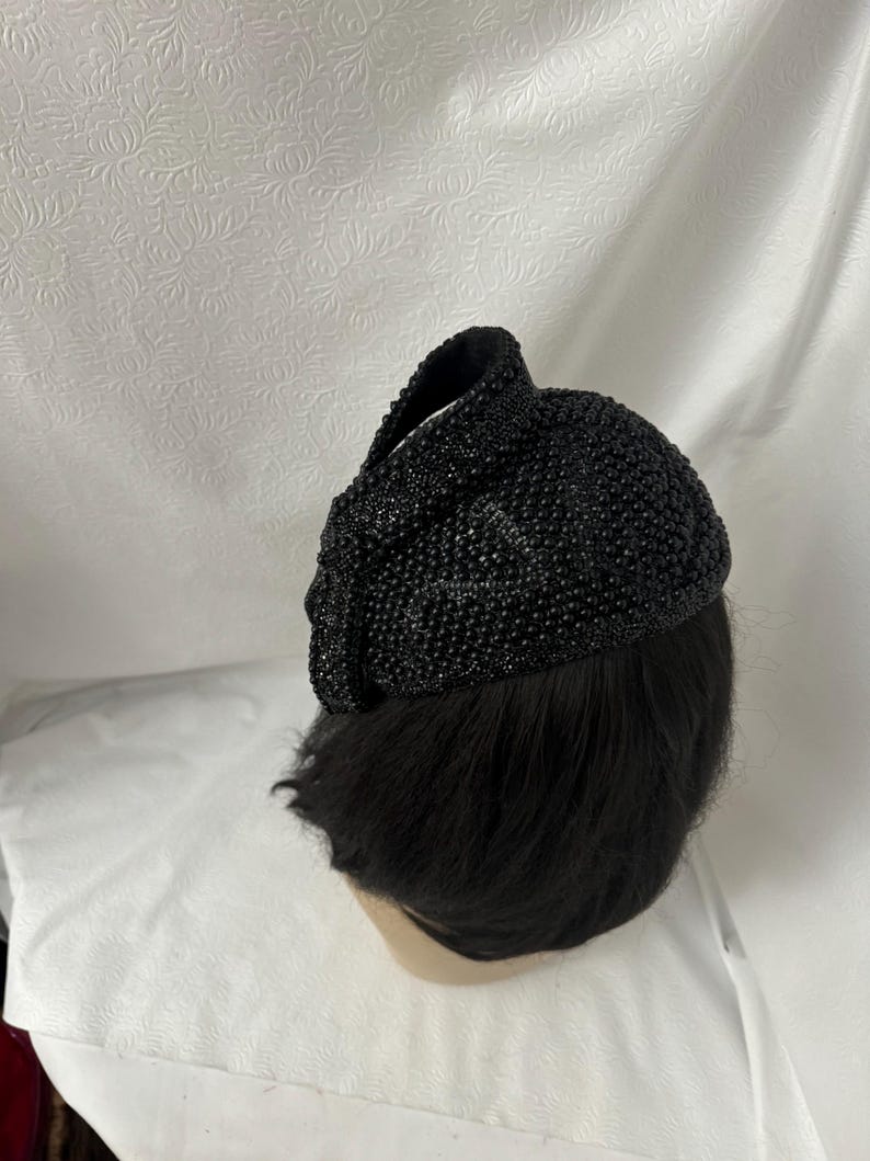 May include: A black beaded hat with a rounded shape. The hat is made of small, black beads that are sewn together.