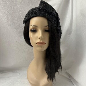 May include: A black beaded hat with a bow on the side. The hat is angled on a mannequin head with black hair.