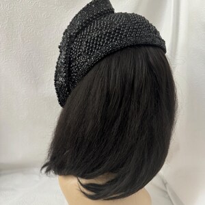 May include: A black beaded hat with a unique design. The hat is made of small, round beads that are sewn together to create a textured surface. The hat is worn on a mannequin with black hair.